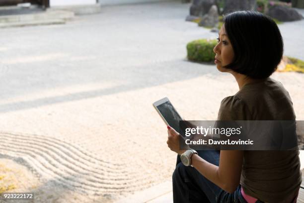 seitenansicht der frau sitzen und mit blick auf tablet im zen-garten von chion-ji-tempel in kyoto, japan - kumikomini stock-fotos und bilder