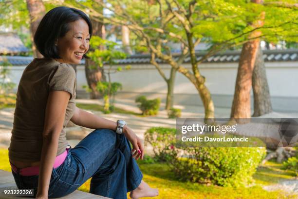 zijaanzicht van de vrouw zitten op het podium van de tempel, glimlachen en te genieten van zen tuin van chion-ji tempel in kyoto, japan - kumikomini stockfoto's en -beelden