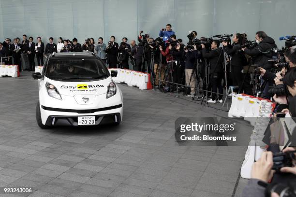 Members of the media take photographs and film a Nissan Motor Co. Leaf electric operated by the "Easy Ride" robot taxi service, a joint development...