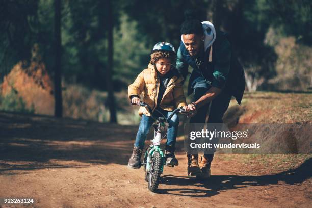 young father teaching son how to ride bicycle in park - family riding bikes with helmets stock pictures, royalty-free photos & images