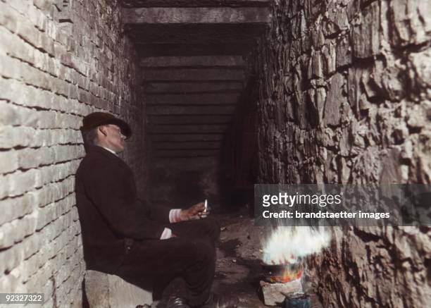 Homeless person sitting by the fire. From the lecture: Durch die Wiener Quartiere des Elends und Verbrechens. Photograph by Hermann Drawe. Vienna....