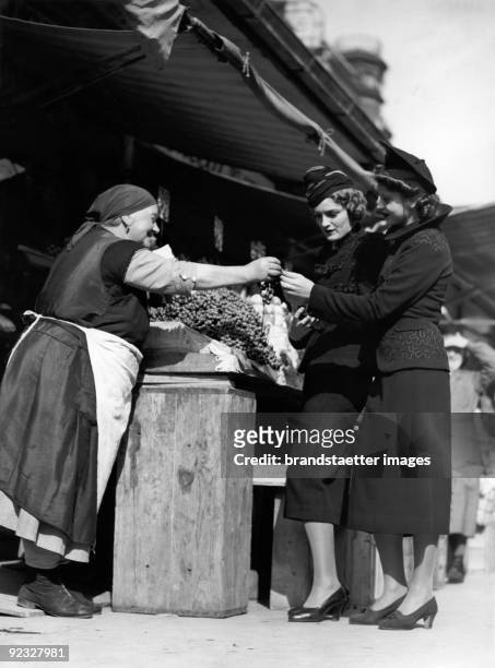 Fashion photography: At a fruit and veg stall. Naschmarkt. Vienna. Photograph. Around 1936.