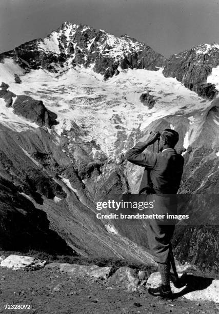 Mountain guide aiming his field glasses at the glacier of the Großer Loeffler. Zillertal Alps. Tyrol. Photograph. Around 1940.