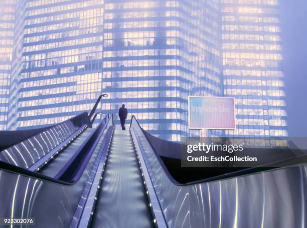 businessman on top of moving escalator at illuminated business district - welvaart stockfoto's en -beelden