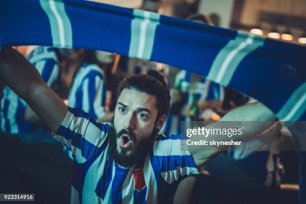 dedicated sports fan cheering for his team while watching a game on tv at home. - supporter scarf stock pictures, royalty-free photos & images