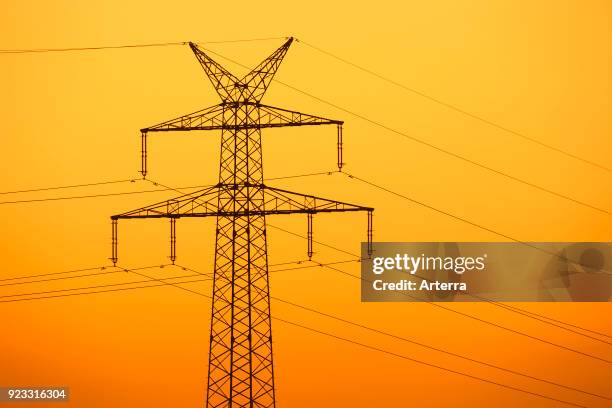 High-voltage electricity pylon - transmission tower silhouetted against sunset.