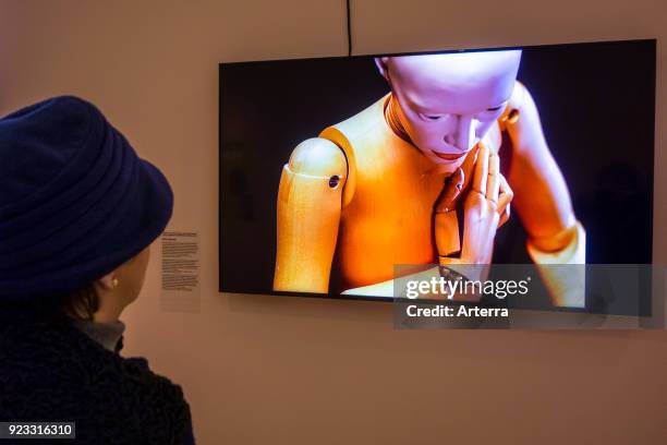 Elderly woman looking at television screen showing female android - humanoid robot at exposition about robotics and artificial intelligence - AI.