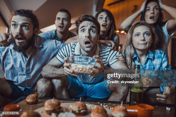 large group of young people watching a sports game on tv at home. - 2018 futures game stock pictures, royalty-free photos & images