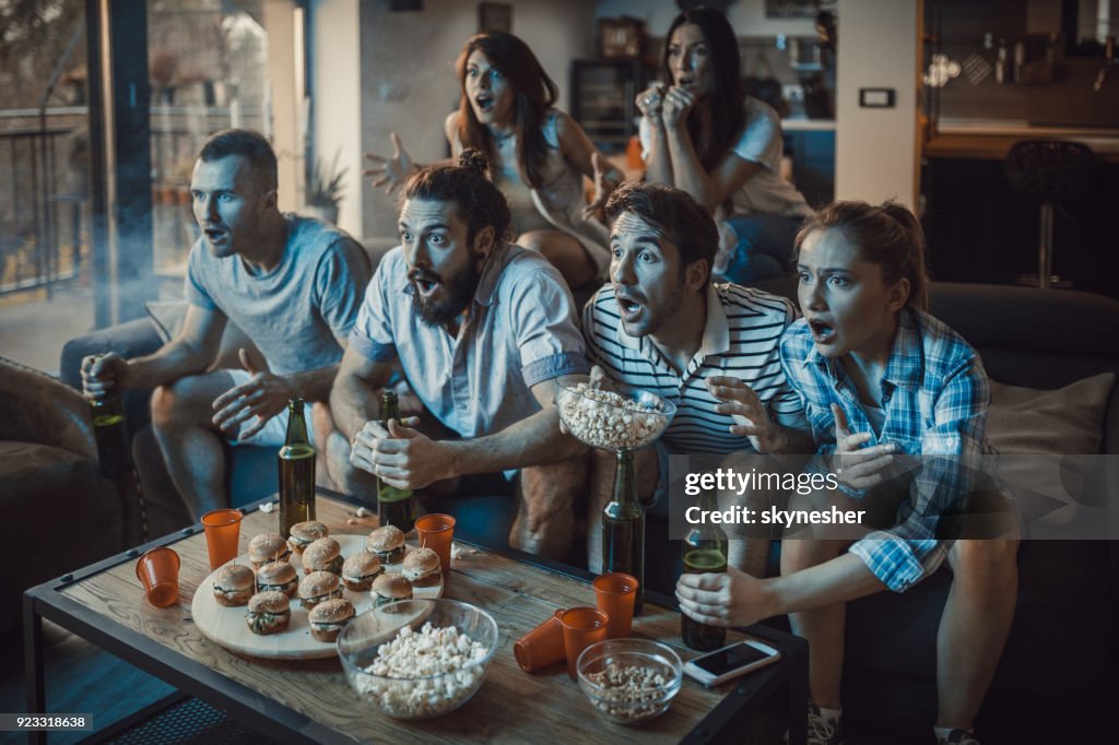 Large group of sports fans watching a game on TV at home.