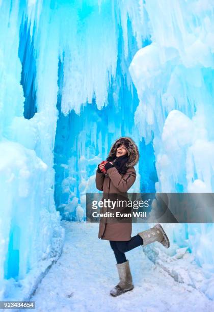 young woman holding a red cup in a parka outside in the cold by ice kicking her leg up smiling - edmonton winter stock pictures, royalty-free photos & images