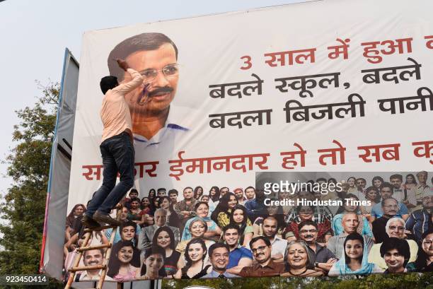 An activist of Bharatiya Janata Yuva Morcha puts black ink on the hoarding of Delhi Chief Minister Arvind Kejriwal which highlights the work of Aam...