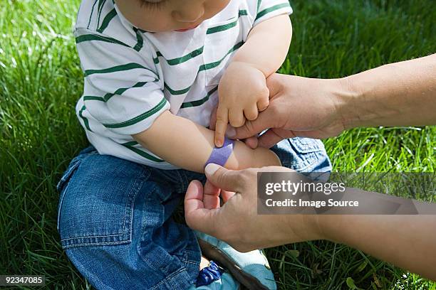 adult putting plaster on baby boy - medical dressing stock pictures, royalty-free photos & images