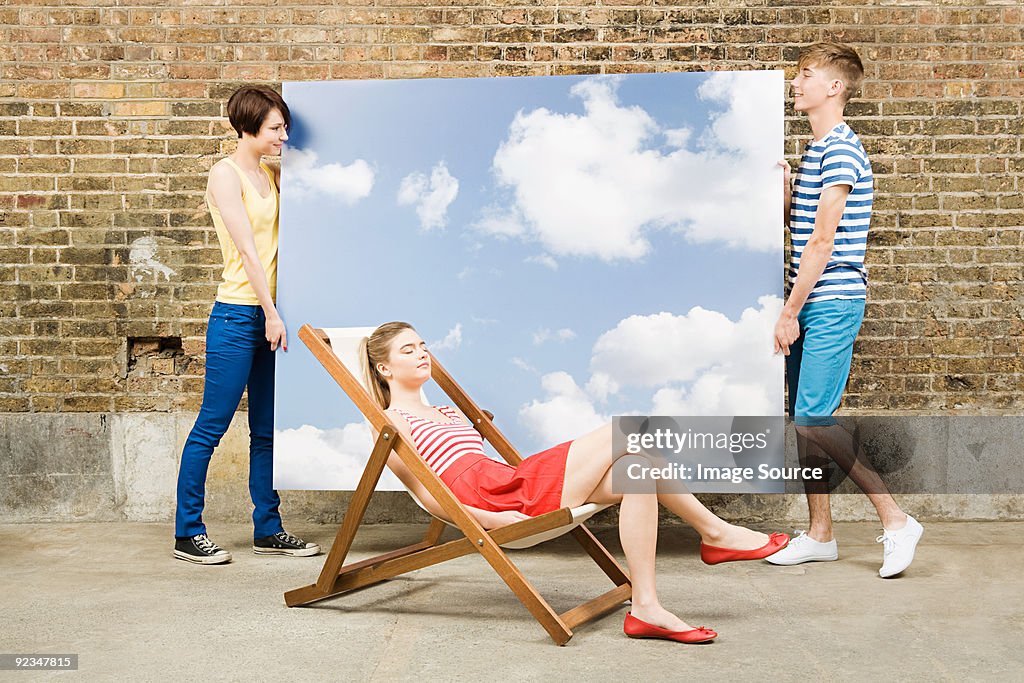 Young woman in deckchair and others with sky backdrop