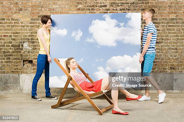 young woman in deckchair and others with sky backdrop - girls sunbathing stock pictures, royalty-free photos & images