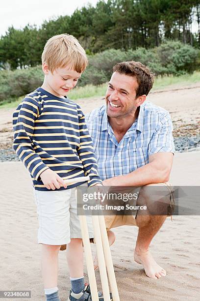 father and son on beach with cricket stumps - family cricket stockfoto's en -beelden