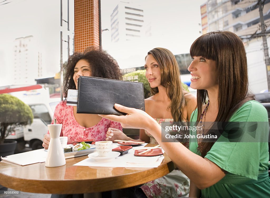 Woman hands credit card to waiter in restaurant.