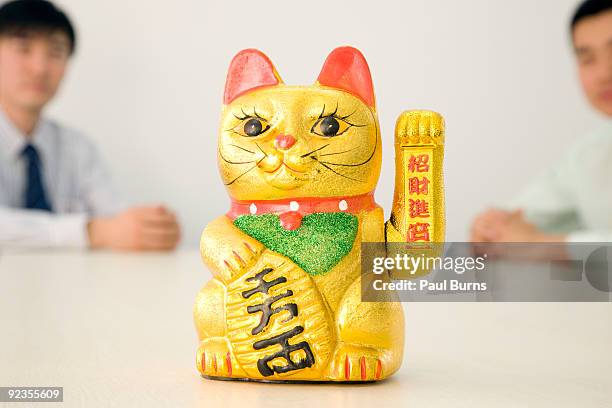 a japanese beckoning cat sitting on a table - maneki neko stock pictures, royalty-free photos & images