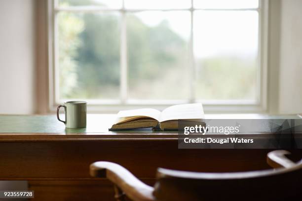 book and mug on traditional writing desk beside window. - antique desk stock pictures, royalty-free photos & images