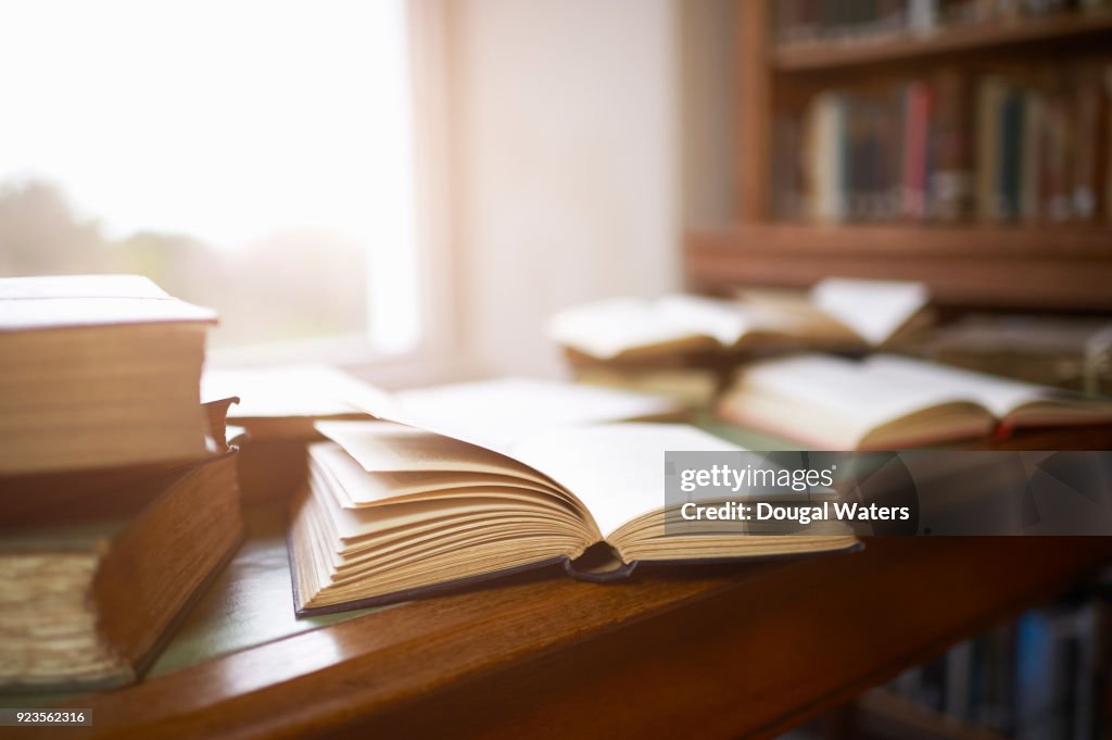 Open vintage books on library desk beside window.