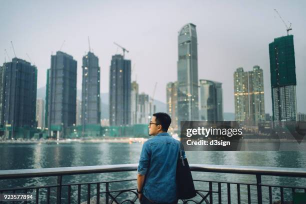 rear view of young man looking at cityscape by the harbour - travel market asia stock-fotos und bilder