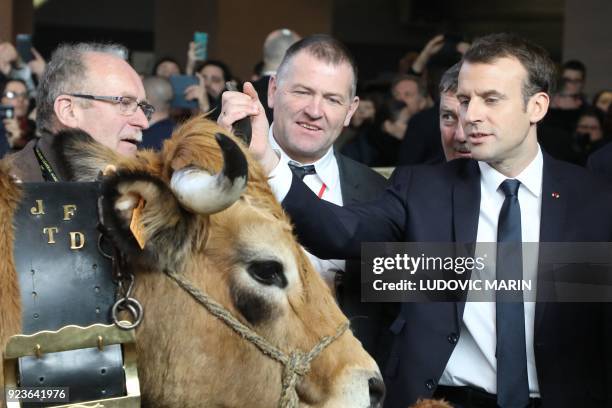 French President Emmanuel Macron touches an Aubrac cow as he visits the 55th International Agriculture Fair at the Porte de Versailles exhibition...