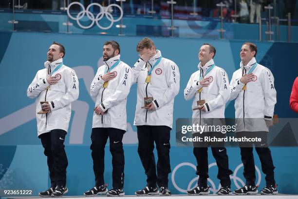 Gold medalists the United States look on during the national anthem in the victory ceremony following the Curling Men's Gold Medal game on day...