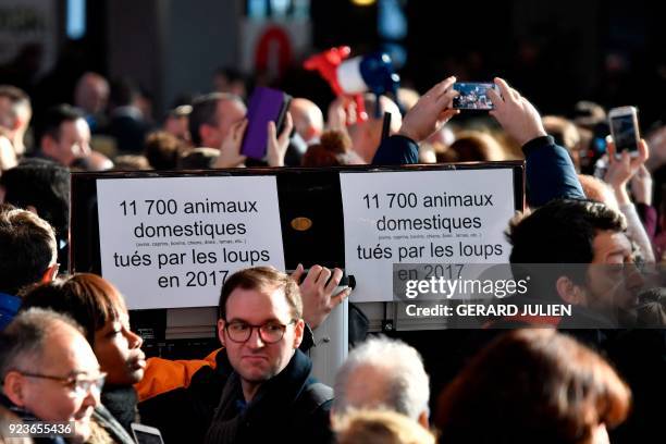People take photographs of French President behind banners reading "11 700 domestic animals killed by wolves in 2017" as he visits the 55th...
