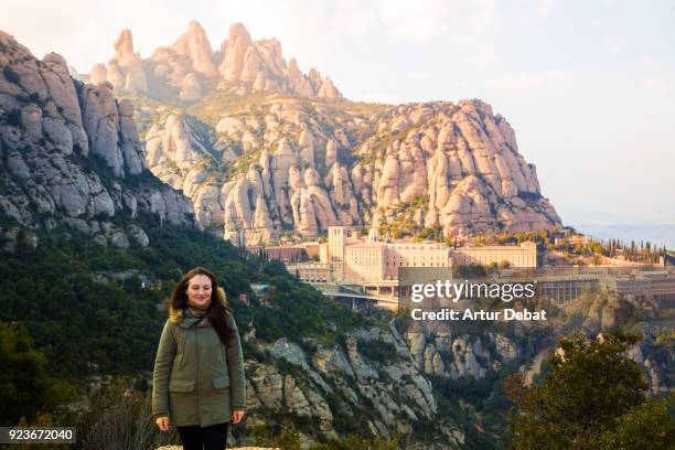 traveler woman feeling the place with eyes closed in front of the monastery of montserrat between the stunning rock formations mountain in catalonia. - montserrat spanje stockfoto's en -beelden