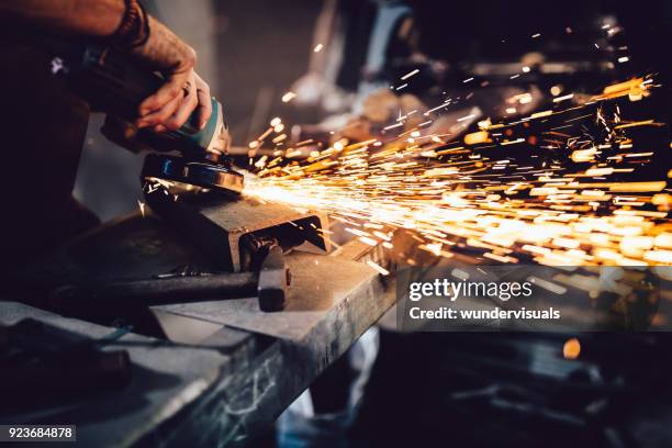 blacksmith working with power tools and metals in workshop - serralheiro imagens e fotografias de stock