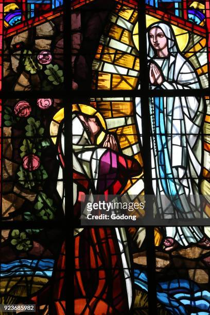 Dalat cathedral. Stained glass window. Our Lady of Lourdes: An image depicting Mary appearing on the grotto, in front of Bernadette Soubirous. Dalat,...