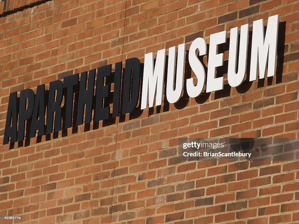 Black and white sign reading Apartheid Museum on brick