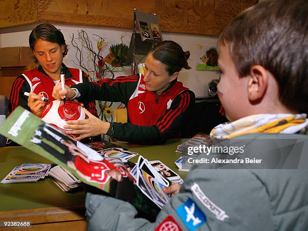 Defenders Sonja Fuss and Annike Krahn of the women's German national soccer team sign autographs on a soccer ball during their visit at an elementary...