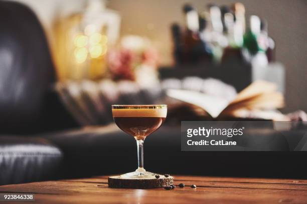 espresso martini cocktail in indoor-einstellung mit kaffeebohnen und buch auf couchtisch - martini glass stock-fotos und bilder