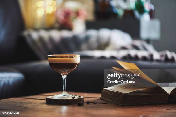 espresso martini cocktail in indoor setting with coffee beans and book on coffee table - espresso martini stock pictures, royalty-free photos & images