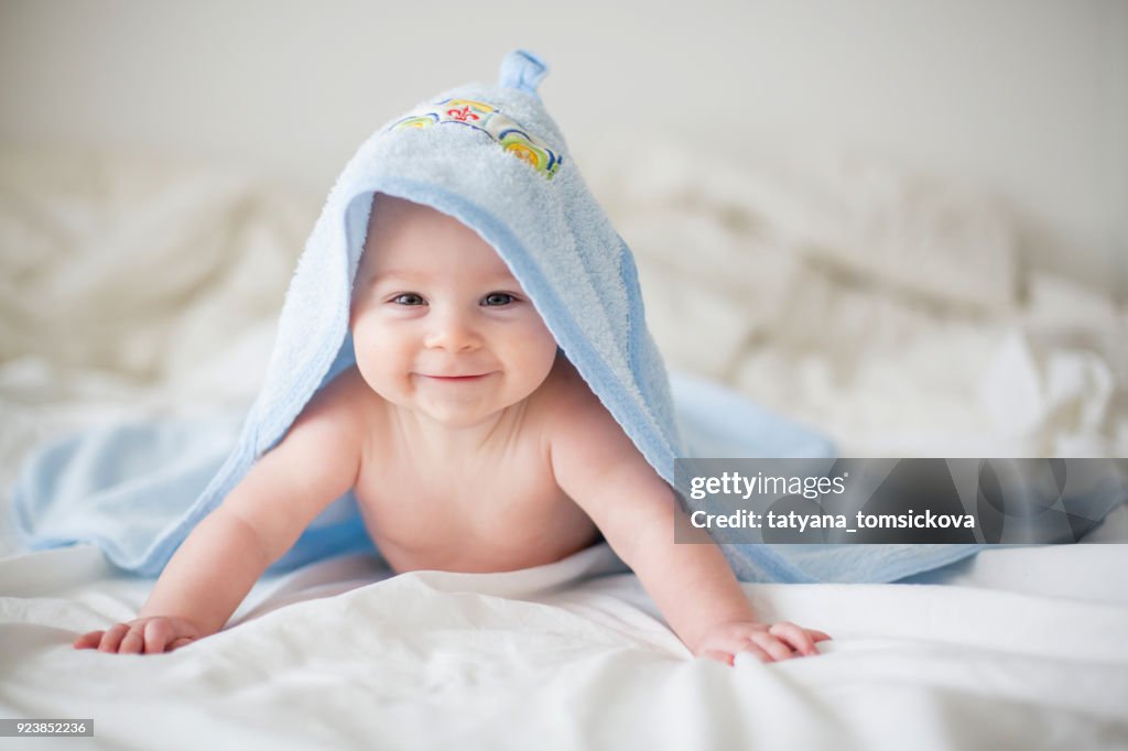 Lindo bebé niño, relajante en la cama después del baño, sonriendo alegremente