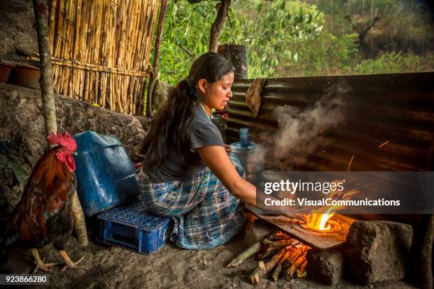 young woman cooking over fire in front of her house. - lake atitlan stock pictures, royalty-free photos & images