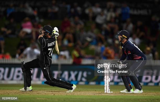 New Zealand batsman Mitchell Santner hits a six as Jos Buttler looks on during the 1st ODI between New Zealand and England at Seddon Park on February...