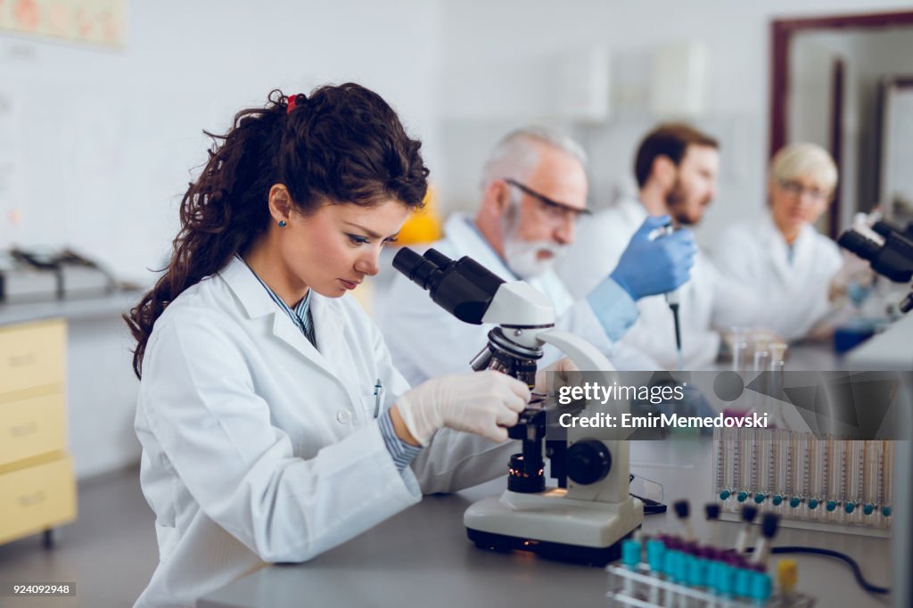 Young female scientist using microscope