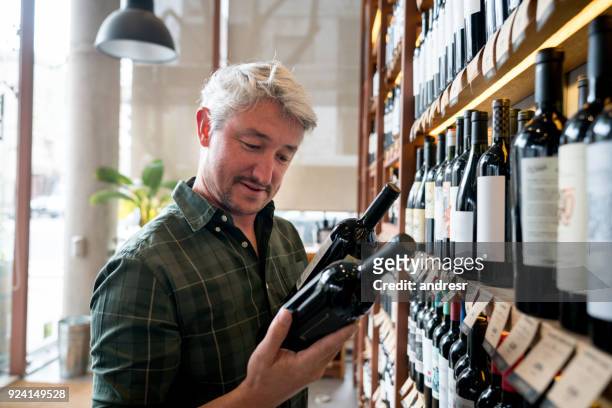 cheerful man at a wine store choosing wines and reading the labels happy - liquor store stock pictures, royalty-free photos & images