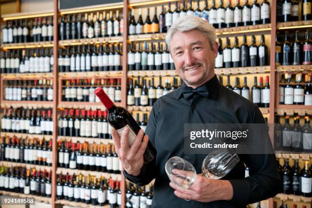 ober in een restaurant houdt een fles wijn en wijnglazen kijken camera glimlachen - sommelier stockfoto's en -beelden