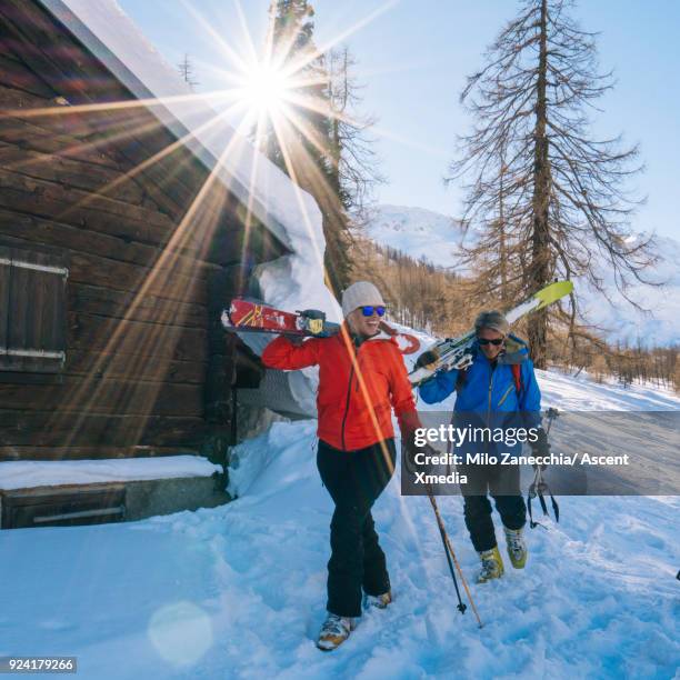 couple backcountry ski past mountain hut after fresh snow - ski boot stock pictures, royalty-free photos & images