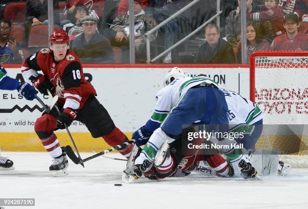 Christian Dvorak of the Arizona Coyotes looks to control the loose puck behind Michael Del Zotto and goalie Jacob Markstrom of the Vancouver Canucks...