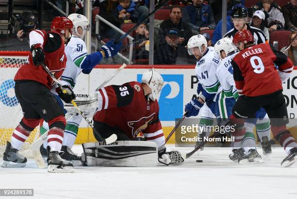 Goalie Darcy Kuemper of the Arizona Coyotes looks to cover the puck as Sven Baertschi and Sam Gagner of the Vancouver Canucks skate in during the...