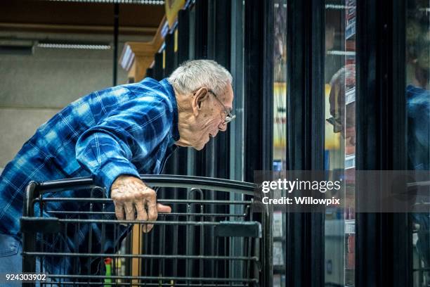 elderly man supermarket grocery shopper looking through refrigerated section cooler window - grocery store window stock pictures, royalty-free photos & images
