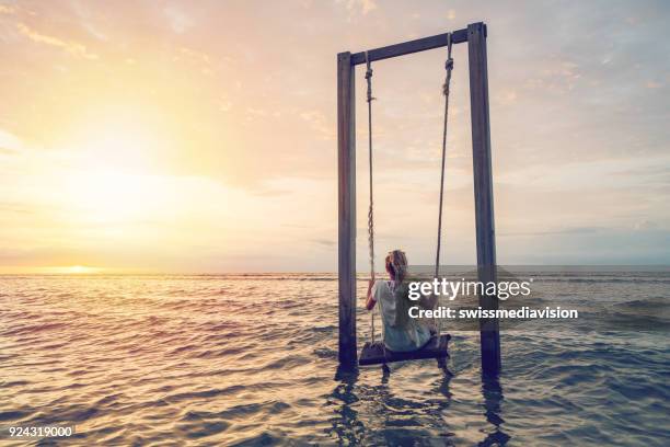 caucasian female playing on swing by the sea at sunset, indonesia - gili trawangan stock pictures, royalty-free photos & images