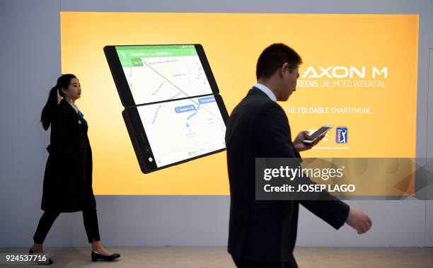 Two people walk past a billboard announcing the new ZTE's dual screens foldable smartphone AXON M on the first day of the Mobile World Congress on...