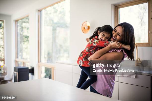 mother and daughter embracing in kitchen - mother daughter kitchen stock-fotos und bilder