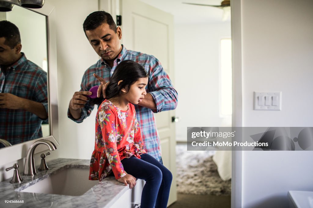 Father brushing daughters hair in bathroom