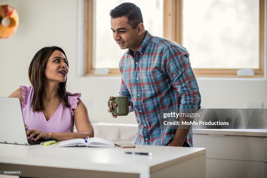 Husband and wife using laptop in kitchen