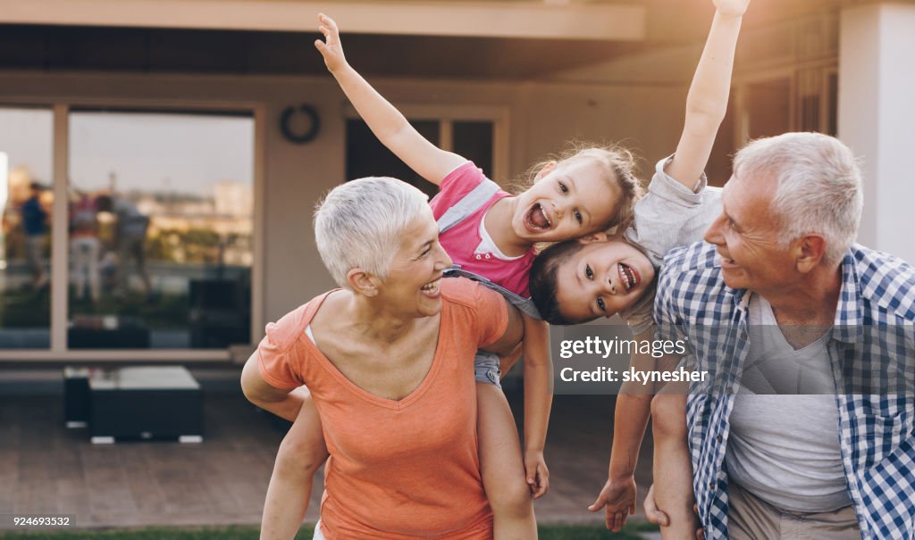 Carefree grandparents piggybacking their joyful grandkids in the front yard.